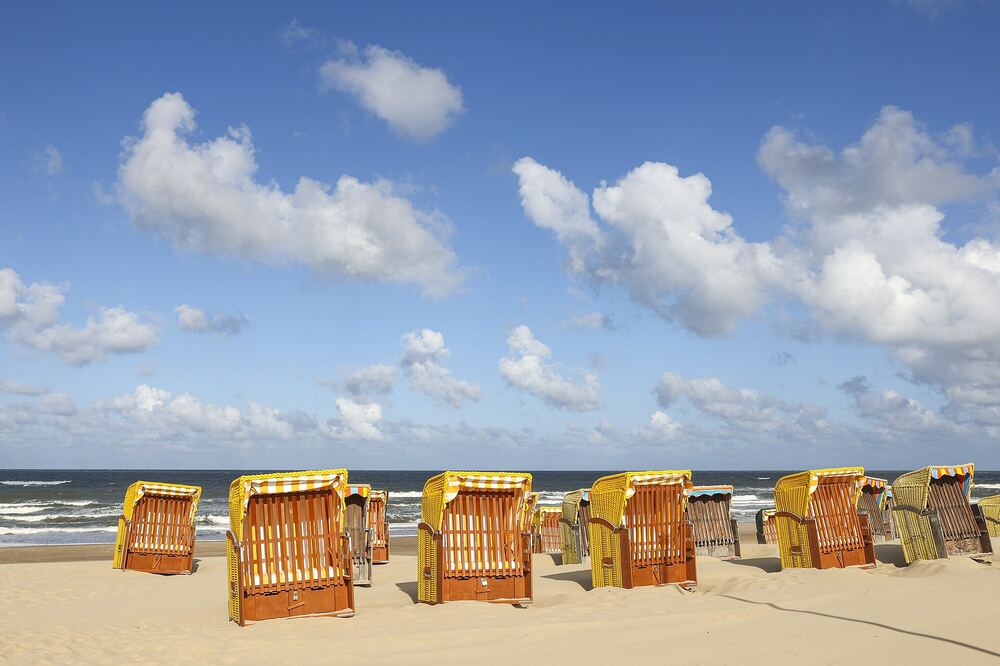Rieten strandstoelen op het strand van Egmond aan Zee met de zee en een wolkenlucht erachter