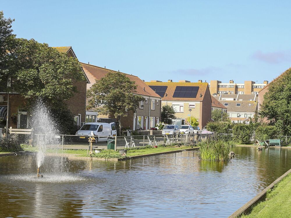 Vijver met fontein in het Winkelmanplantsoen in Egmond aan Zee, met gras en huizen langs het water